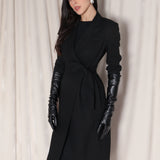 A professional woman wearing a sophisticated black long-sleeve coat dress, featuring an elegant tie-waist belt and notched lapels, styled over a white shirt for a polished executive business look.