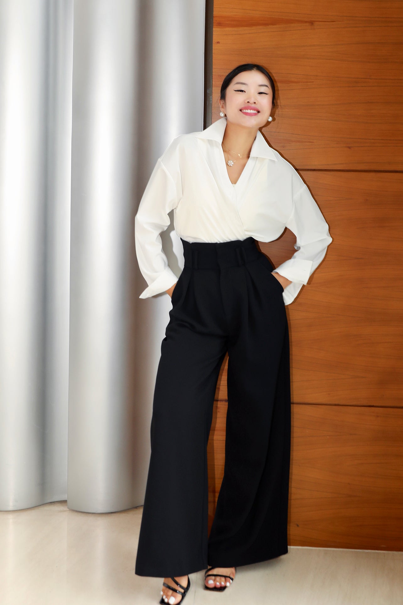 A professional woman wearing sophisticated black high-waisted wide-leg trousers, featuring a flattering high-rise fit and a flowing full-length silhouette for an elegant office look.