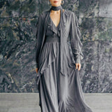 A style comparison of two elegant long-sleeve chiffon maxi dresses; the left showcasing a vibrant purple dress with a deep V-neckline and tiered ruffles along the sleeves, and the right featuring a sophisticated grey version styled with a matching neck scarf and smocked waistband.