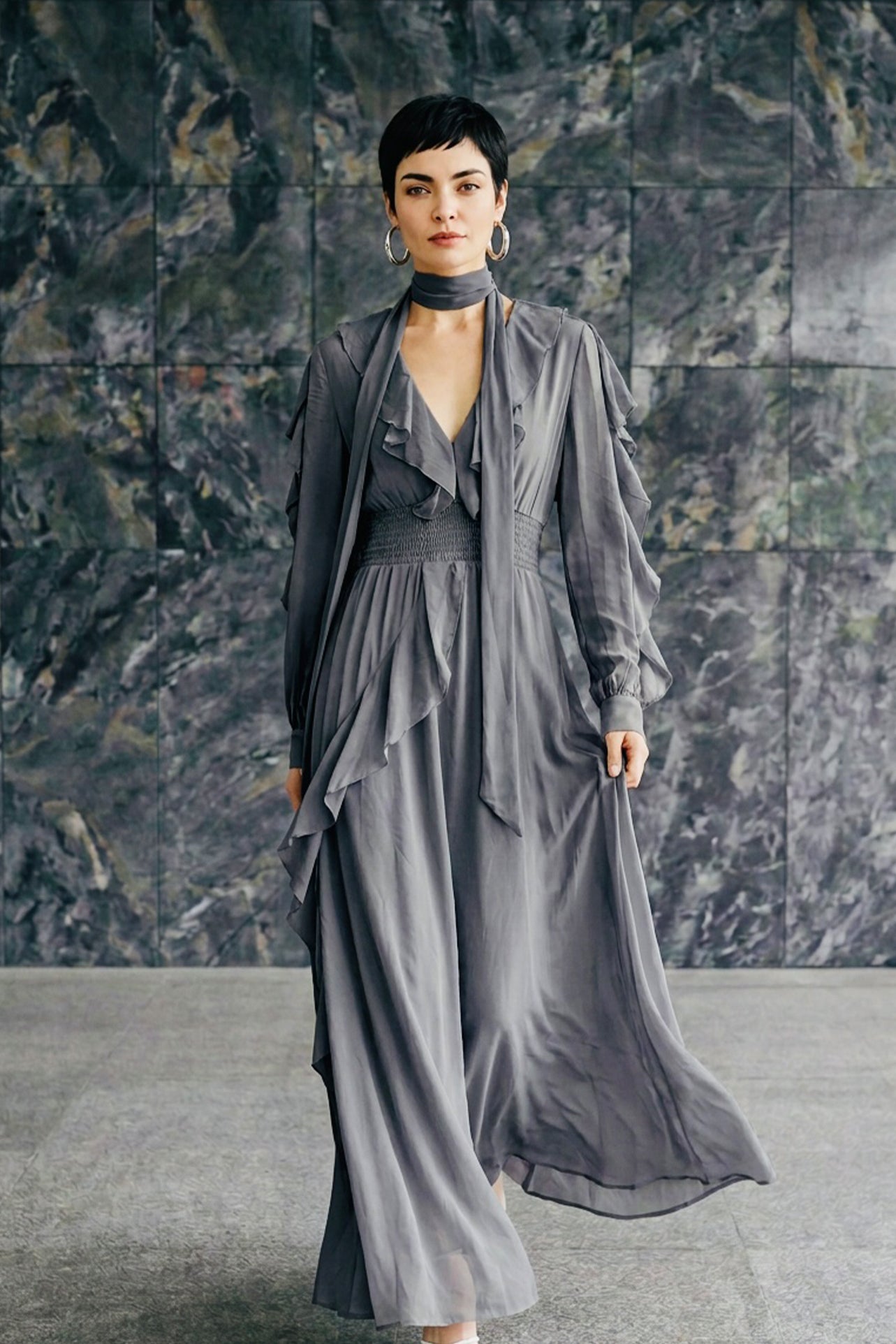 A style comparison of two elegant long-sleeve chiffon maxi dresses; the left showcasing a vibrant purple dress with a deep V-neckline and tiered ruffles along the sleeves, and the right featuring a sophisticated grey version styled with a matching neck scarf and smocked waistband.
