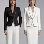 Two elegant professional women modeling high-end monochrome executive suits, one in a black blazer with white piping and wide-leg trousers, the other in a white blazer with dark trim and a matching pencil skirt.