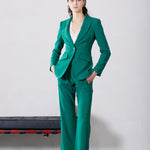 A professional woman wearing a sophisticated emerald green tailored blazer, featuring a slim-fit silhouette, notched lapels, and flap pockets, styled elegantly with a patterned silk scarf for a corporate office look.