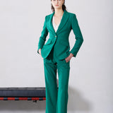 A professional woman wearing a sophisticated emerald green tailored blazer, featuring a slim-fit silhouette, notched lapels, and flap pockets, styled elegantly with a patterned silk scarf for a corporate office look.
