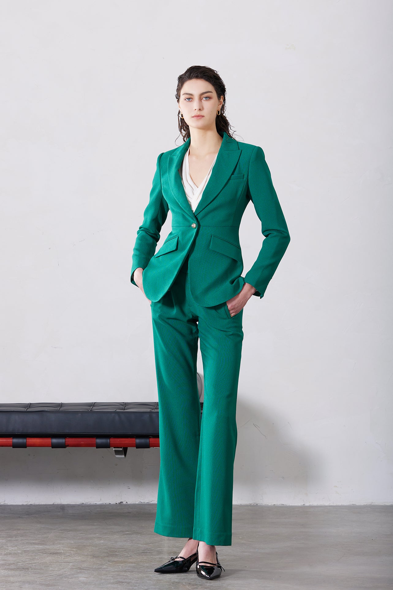 A professional woman wearing a sophisticated emerald green tailored blazer, featuring a slim-fit silhouette, notched lapels, and flap pockets, styled elegantly with a patterned silk scarf for a corporate office look.