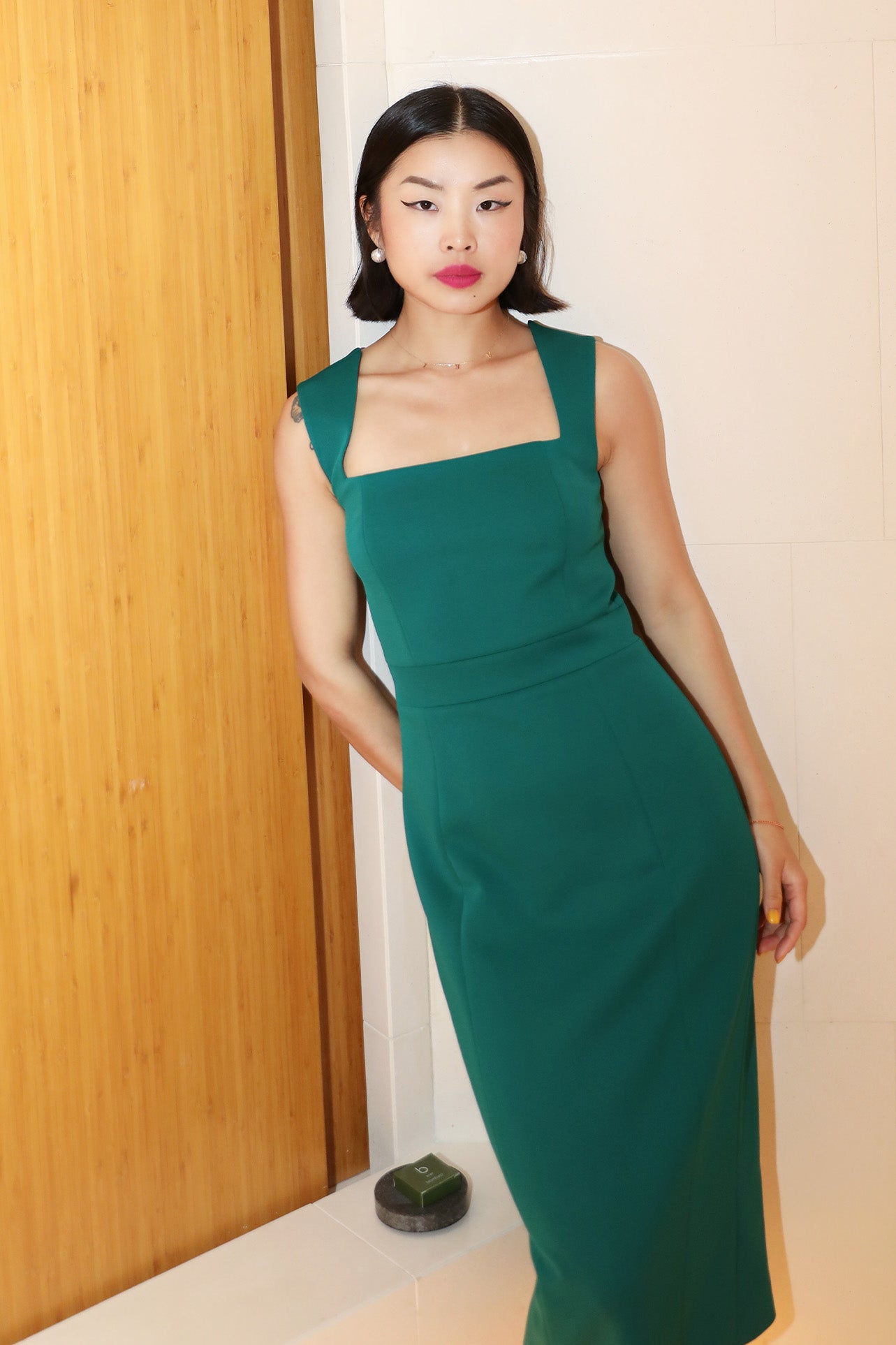 A professional woman wearing a sophisticated emerald green sleeveless dress, featuring a classic square neckline and a flattering tailored sheath silhouette for an elegant executive look.