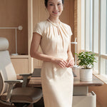 A professional woman modeling a sophisticated blush pink sheath dress, featuring a unique gathered neckline with keyhole detail and a tailored slim fit for a timeless executive look.