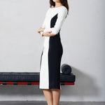 A professional woman wearing a sophisticated black and white color-block midi dress, featuring slimming side panels, long sleeves, and an elegant black belt with a gold buckle for a modern executive office look.