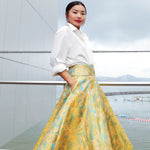 A professional woman wearing a sophisticated high-waisted A-line skirt, featuring a luxurious gold and teal wave pattern jacquard fabric and elegant full-skirt volume for a formal event.