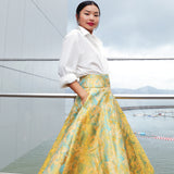 A professional woman wearing a sophisticated high-waisted A-line skirt, featuring a luxurious gold and teal wave pattern jacquard fabric and elegant full-skirt volume for a formal event.