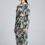 A professional woman wearing a sophisticated dark green wrap dress with a vibrant pink floral print, featuring long sleeves and a slimming waist-tie for an elegant spring look.
