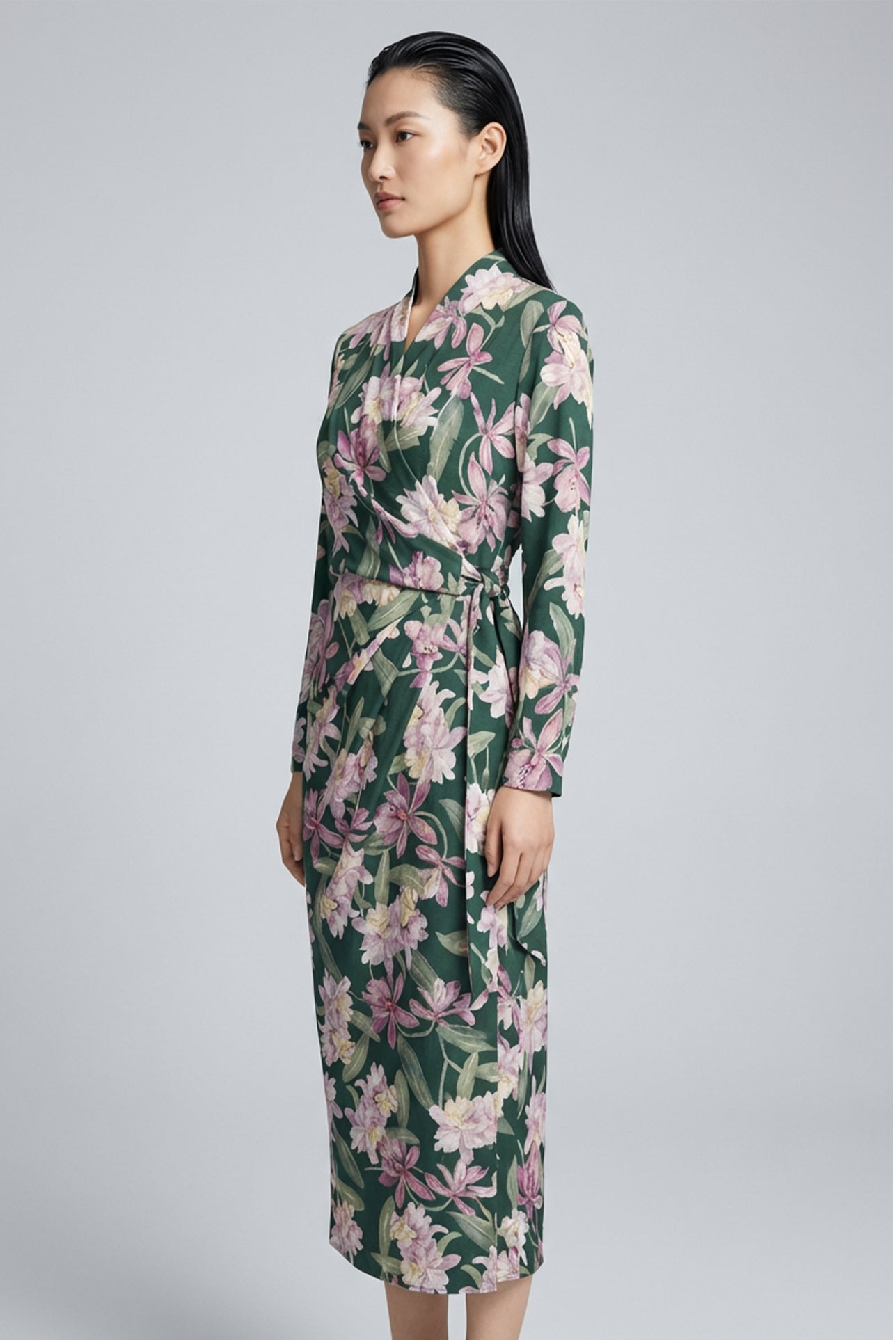 A professional woman wearing a sophisticated dark green wrap dress with a vibrant pink floral print, featuring long sleeves and a slimming waist-tie for an elegant spring look.