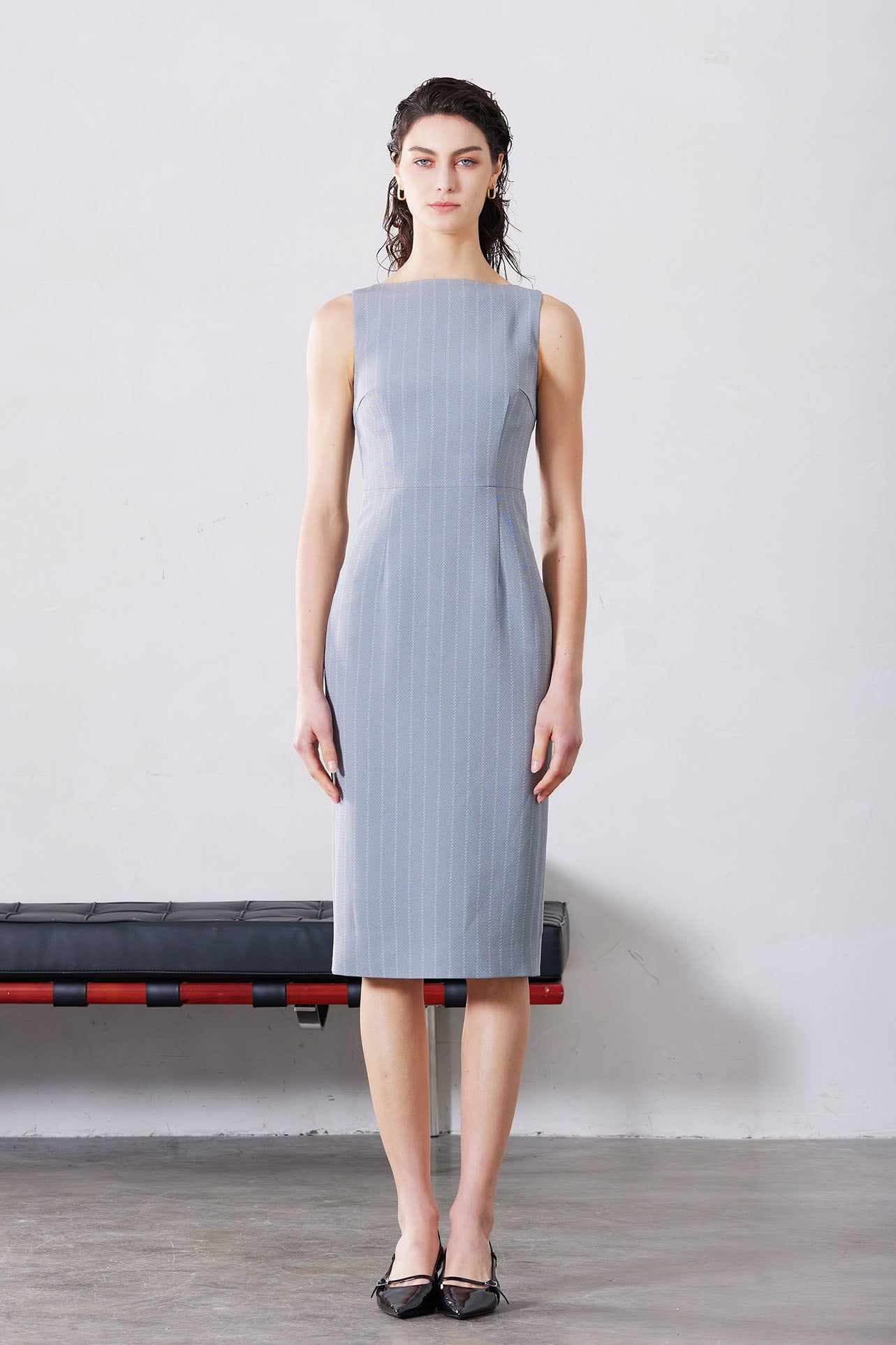 A professional woman wearing a sophisticated light grey pinstripe sleeveless sheath dress, featuring an elegant boat neckline and a tailored slim-fit silhouette for a polished executive look.