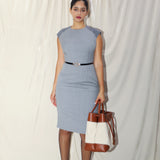 A professional woman wearing a sophisticated grey sleeveless sheath dress, featuring a tailored slim-fit silhouette and an elegant thin black belt with a gold buckle for a polished executive office look.