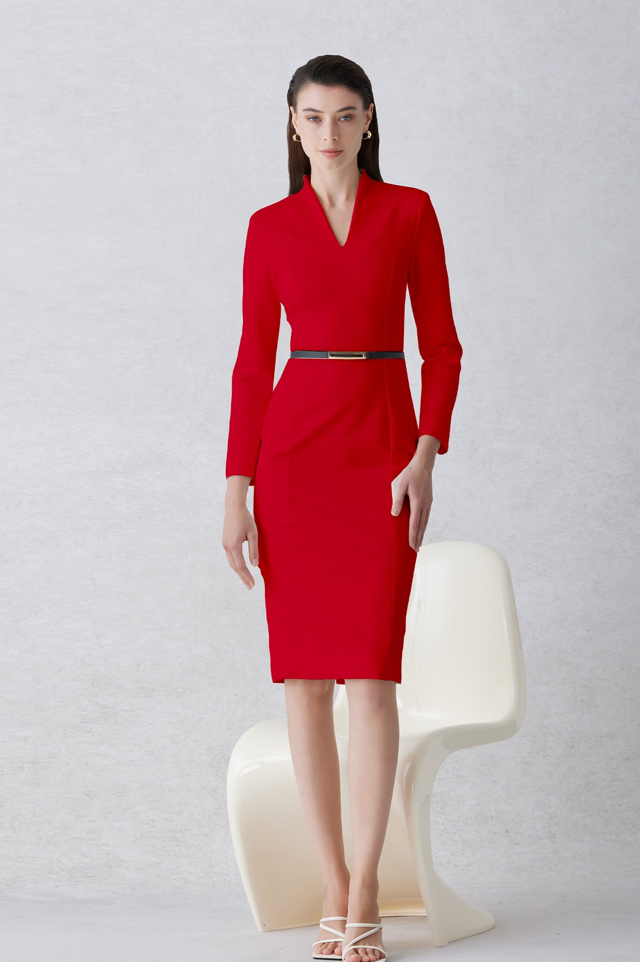 A professional woman wearing a sophisticated solid white long-sleeve sheath dress, featuring an elegant V-neckline and a slim black belt with a gold buckle for a polished executive office look.
