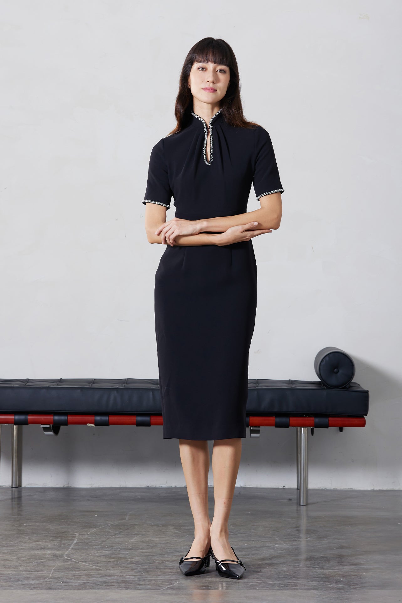 An elegant woman wearing a sophisticated black short-sleeve sheath dress, featuring a traditional mandarin collar with a modern keyhole neckline and delicate beaded trim details for a polished formal look.