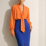 A style collection of three models presenting elegant dopamine office wear; the left in a white bow-tie blouse with a mustard yellow front-slit midi skirt, the center wearing a blue striped pussy-bow shirt with a straw hat and white wide-leg trousers, and the right in a vibrant orange satin blouse with a royal blue pencil skirt