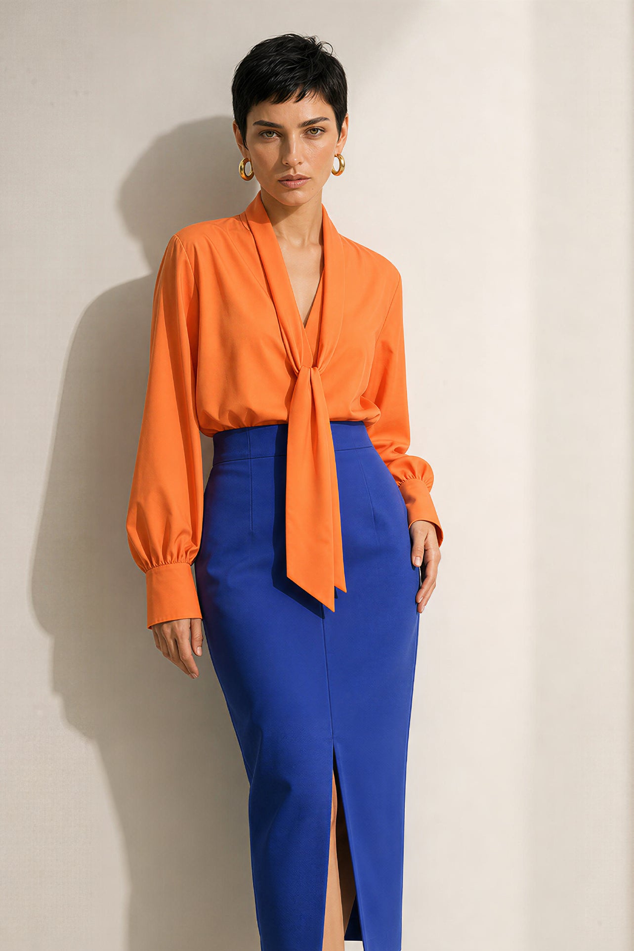 A style collection of three models presenting elegant dopamine office wear; the left in a white bow-tie blouse with a mustard yellow front-slit midi skirt, the center wearing a blue striped pussy-bow shirt with a straw hat and white wide-leg trousers, and the right in a vibrant orange satin blouse with a royal blue pencil skirt