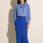 A style comparison of two elegant tailored midi pencil skirts with a sharp front slit; the left showcasing a vibrant royal blue high-waisted skirt paired with a striped shirt, and the right featuring a rich mustard yellow version paired with a bright orange blouse.