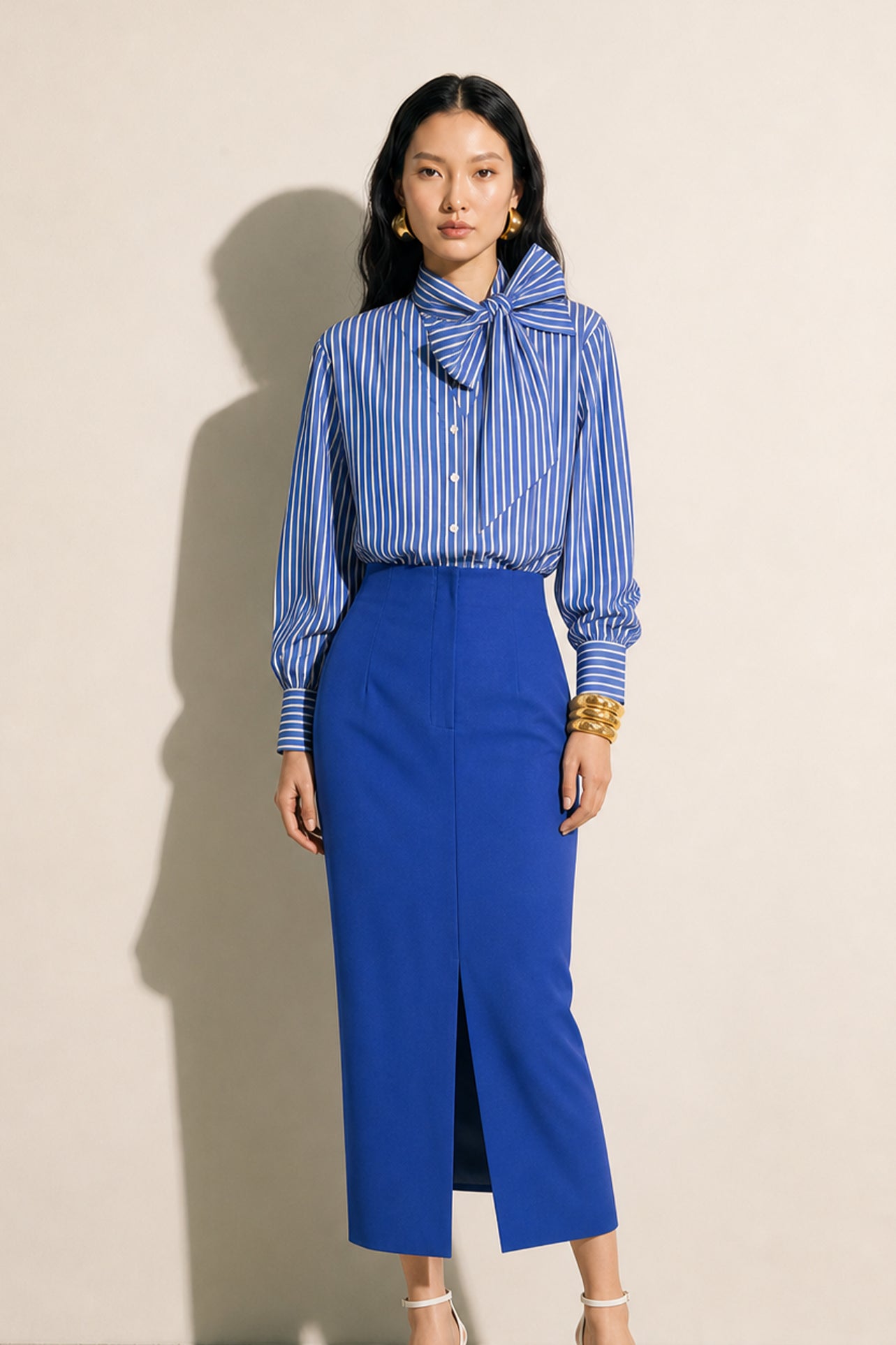 A style comparison of two elegant tailored midi pencil skirts with a sharp front slit; the left showcasing a vibrant royal blue high-waisted skirt paired with a striped shirt, and the right featuring a rich mustard yellow version paired with a bright orange blouse.