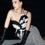 A professional woman wearing a sophisticated one-shoulder black and white floral print top, featuring a dramatic oversized bow detail on the shoulder, paired with white high-waisted trousers for an elegant evening look.