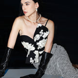 A professional woman wearing a sophisticated one-shoulder black and white floral print top, featuring a dramatic oversized bow detail on the shoulder, paired with white high-waisted trousers for an elegant evening look.
