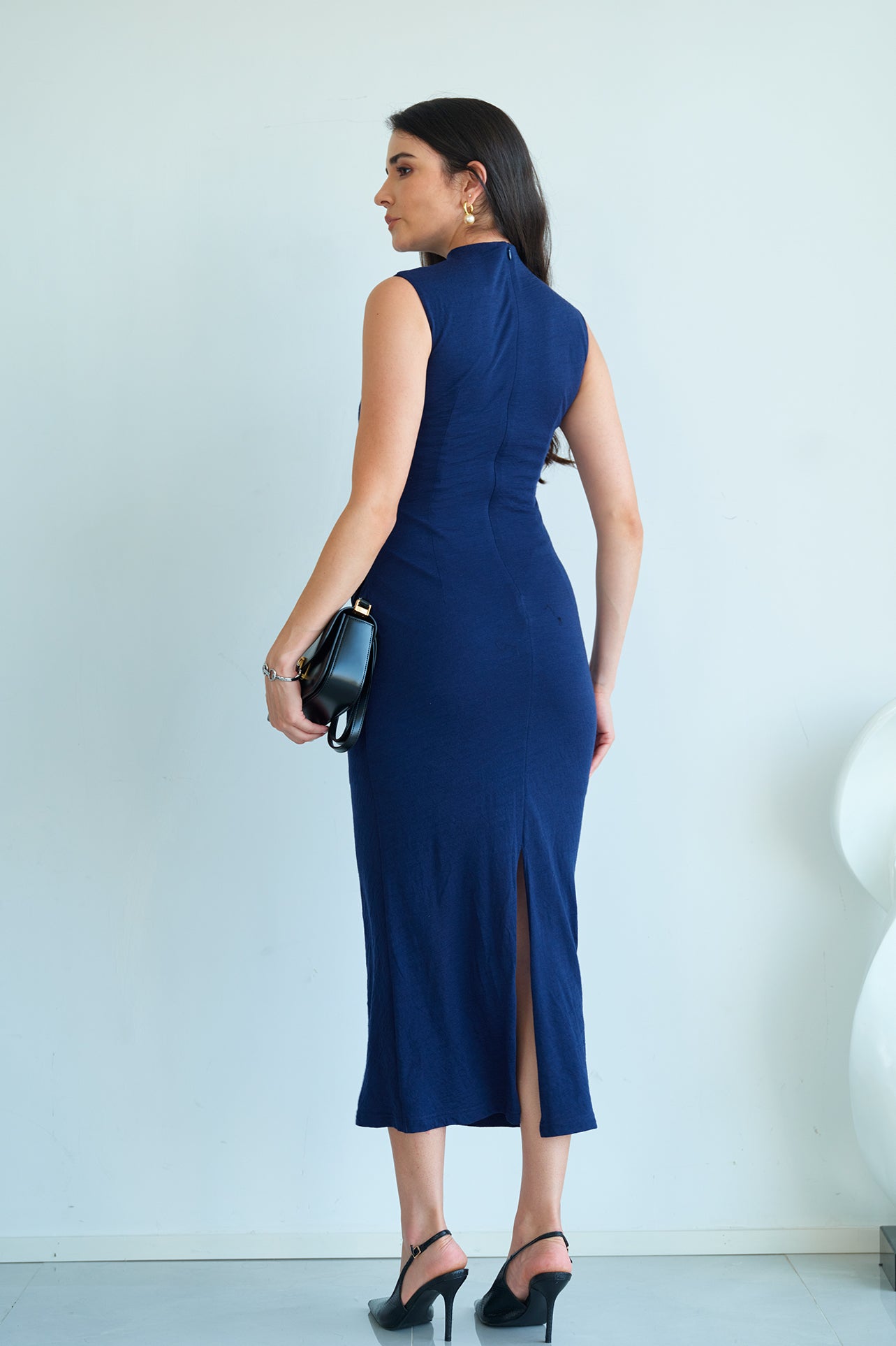 A professional woman wearing a sophisticated navy blue sleeveless midi dress, featuring an elegant high neckline and flattering ruched detailing along the side for a slim-fit executive look.