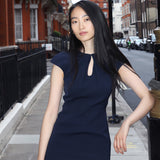 A professional woman wearing a sophisticated navy blue midi dress, featuring an elegant pleated neckline with a subtle keyhole detail and a tailored slim-fit pencil silhouette for a polished executive look.