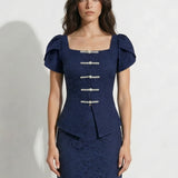 A professional woman modeling an elegant navy blue lace short top, featuring a retro square neckline, romantic short puff sleeves, and a series of pearl and rhinestone frog closures on the front with a tailored triangular split hem, paired with light blue high-waisted jeans.