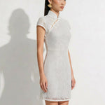 A professional woman modeling an elegant white lace modern qipao dress, featuring an intricate eyelet textured fabric, a sophisticated mandarin collar with a traditional knot button, and slimming cap sleeves.
