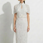 A professional woman modeling an elegant white lace halter neck modern qipao dress, featuring a sophisticated mandarin collar with keyhole detail and an intricate eyelet embroidered fabric for a quiet luxury look.