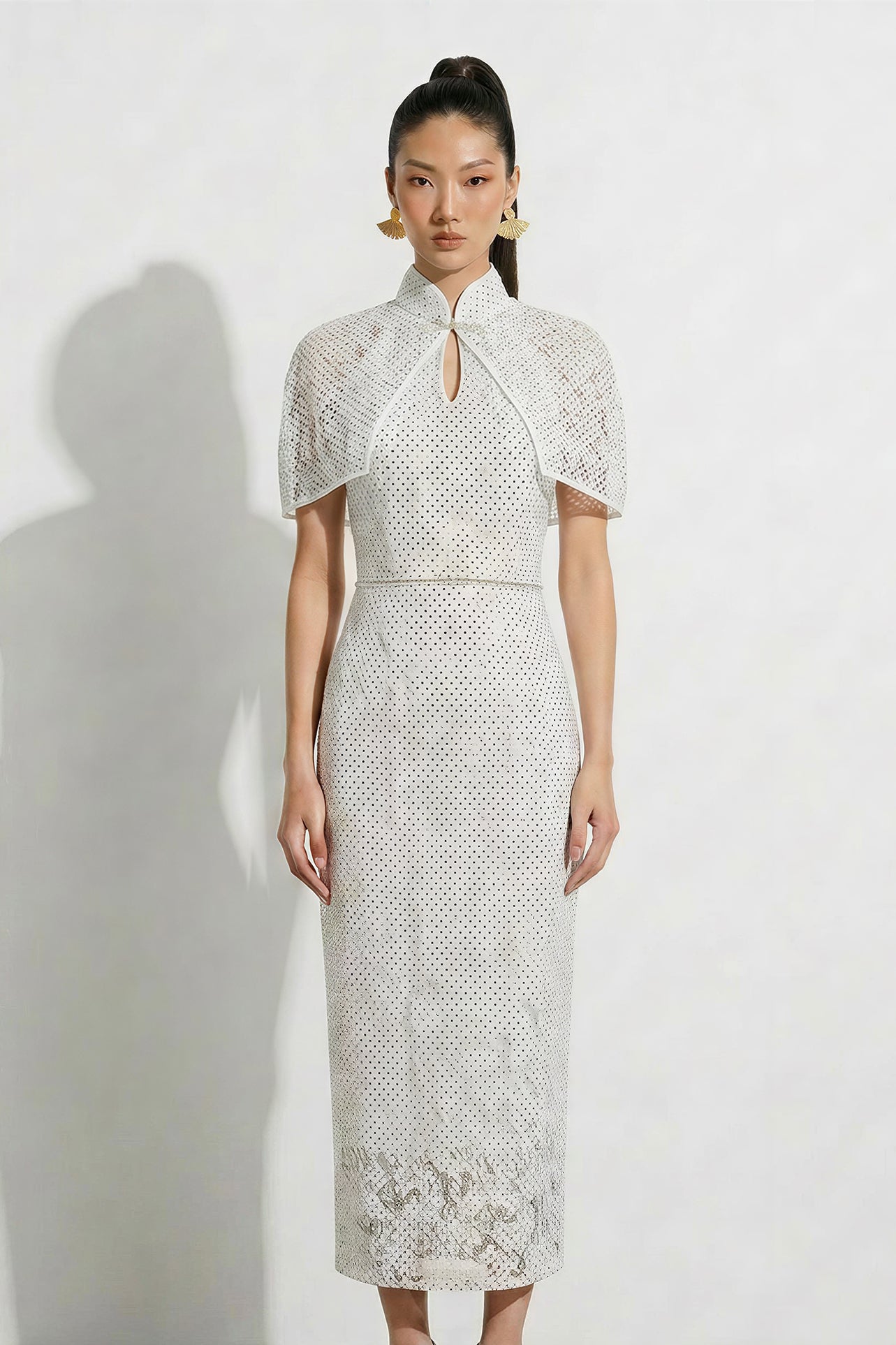 A professional woman modeling an elegant white lace halter neck modern qipao dress, featuring a sophisticated mandarin collar with keyhole detail and an intricate eyelet embroidered fabric for a quiet luxury look.