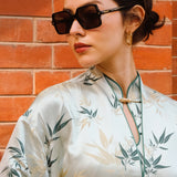 A professional woman modeling an elegant light sage green silk wrap jacket, featuring dark green bamboo leaf prints, a sophisticated mandarin collar with keyhole detail, and wide kimono sleeves.