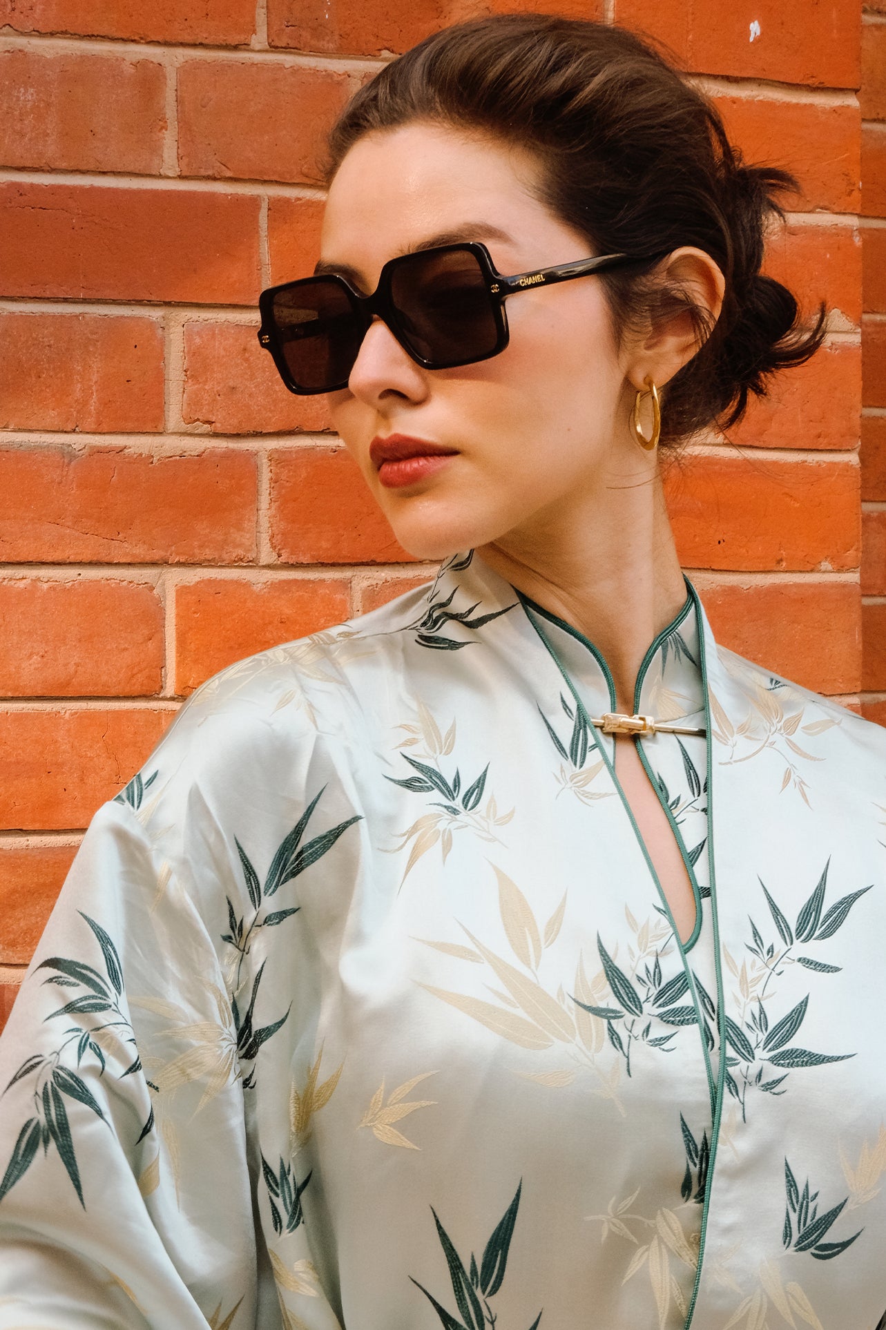 A professional woman modeling an elegant light sage green silk wrap jacket, featuring dark green bamboo leaf prints, a sophisticated mandarin collar with keyhole detail, and wide kimono sleeves.
