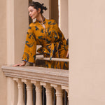 A beautiful woman modeling an elegant mustard yellow modern Chinese jacket, featuring intricate blue phoenix embroidery, a sophisticated mandarin collar, and wide kimono sleeves with a matching waist tie.