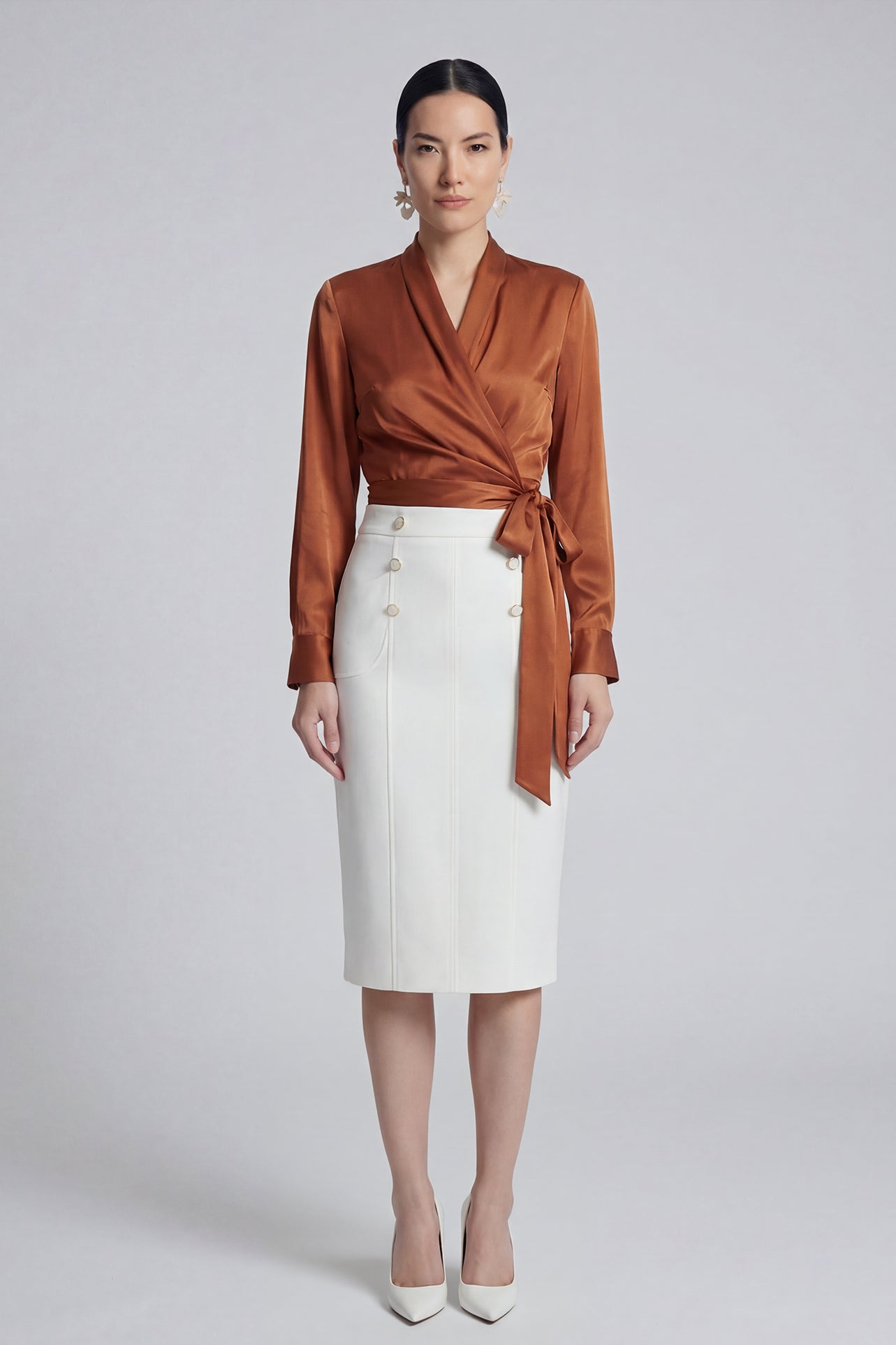 A professional woman wearing a high-end white silk wrap blouse with a side-tie detail, paired with a tailored black high-waisted pencil skirt for a sophisticated executive office look.