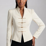 A sophisticated woman enjoying coffee in Paris wearing an elegant cream white modern qipao suit, featuring a mandarin collar blazer with traditional frog buttons and a matching pleated skirt for a quiet luxury oriental look.