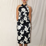 A professional woman wearing a stunning black sleeveless qipao-inspired dress, featuring a chic halter neck with a traditional mandarin collar and large elegant white floral embroidery for a modern oriental evening look.