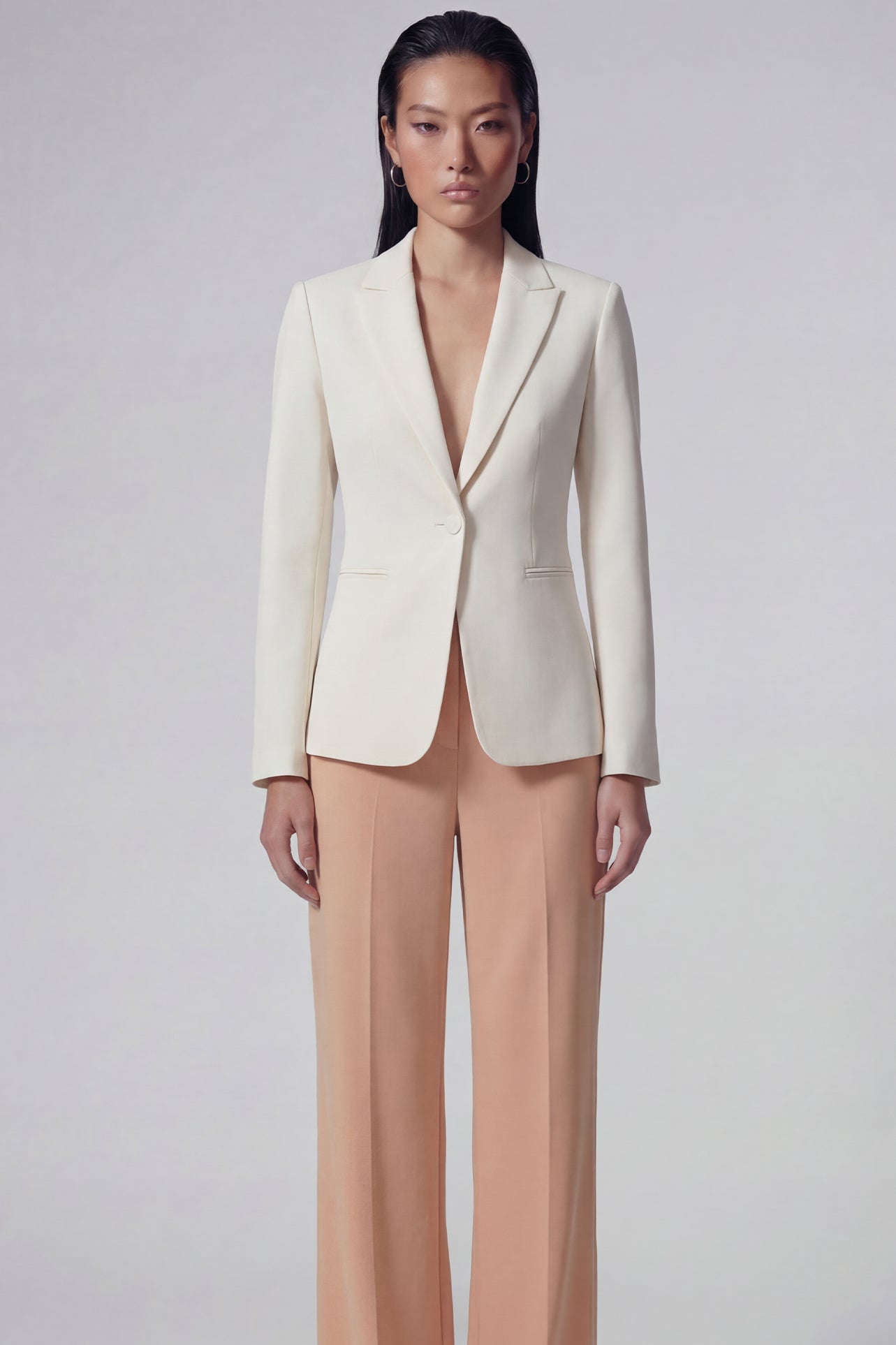 A professional woman wearing sophisticated apricot-colored high-waisted straight-leg trousers, featuring a unique pointed waistband design for a tailored executive office look.