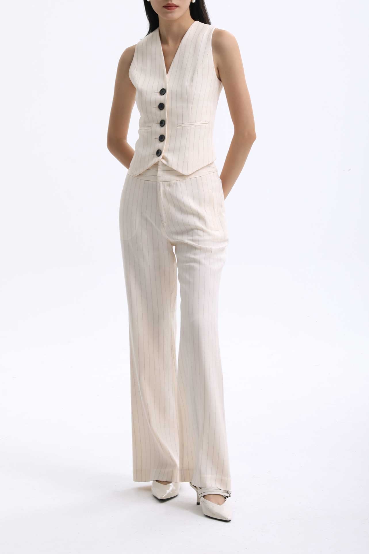 A professional woman wearing sophisticated cream pinstripe high-waisted wide-leg trousers, featuring a tailored loose-fit silhouette and styled with a pearl handbag for an elegant old money office look.