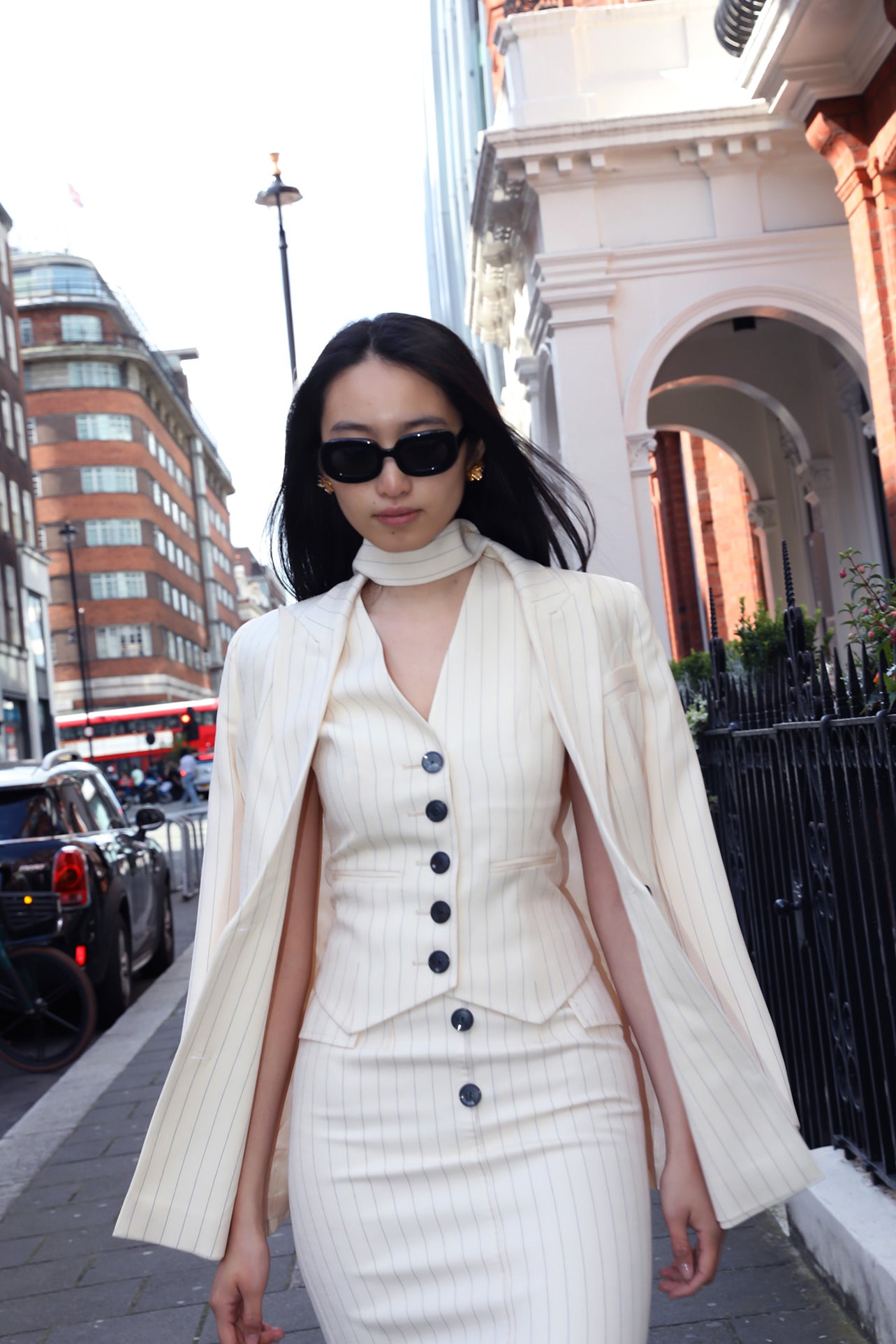 A professional woman wearing a sophisticated cream pinstripe blazer, featuring a double-breasted front with a chic waist-tie belt and notched lapels for a polished old money office look.