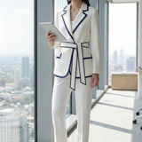 An elegant professional woman wearing a tailored white blazer with navy blue contrast piping, featuring a self-tie belt to define the waist for a smart-casual office look