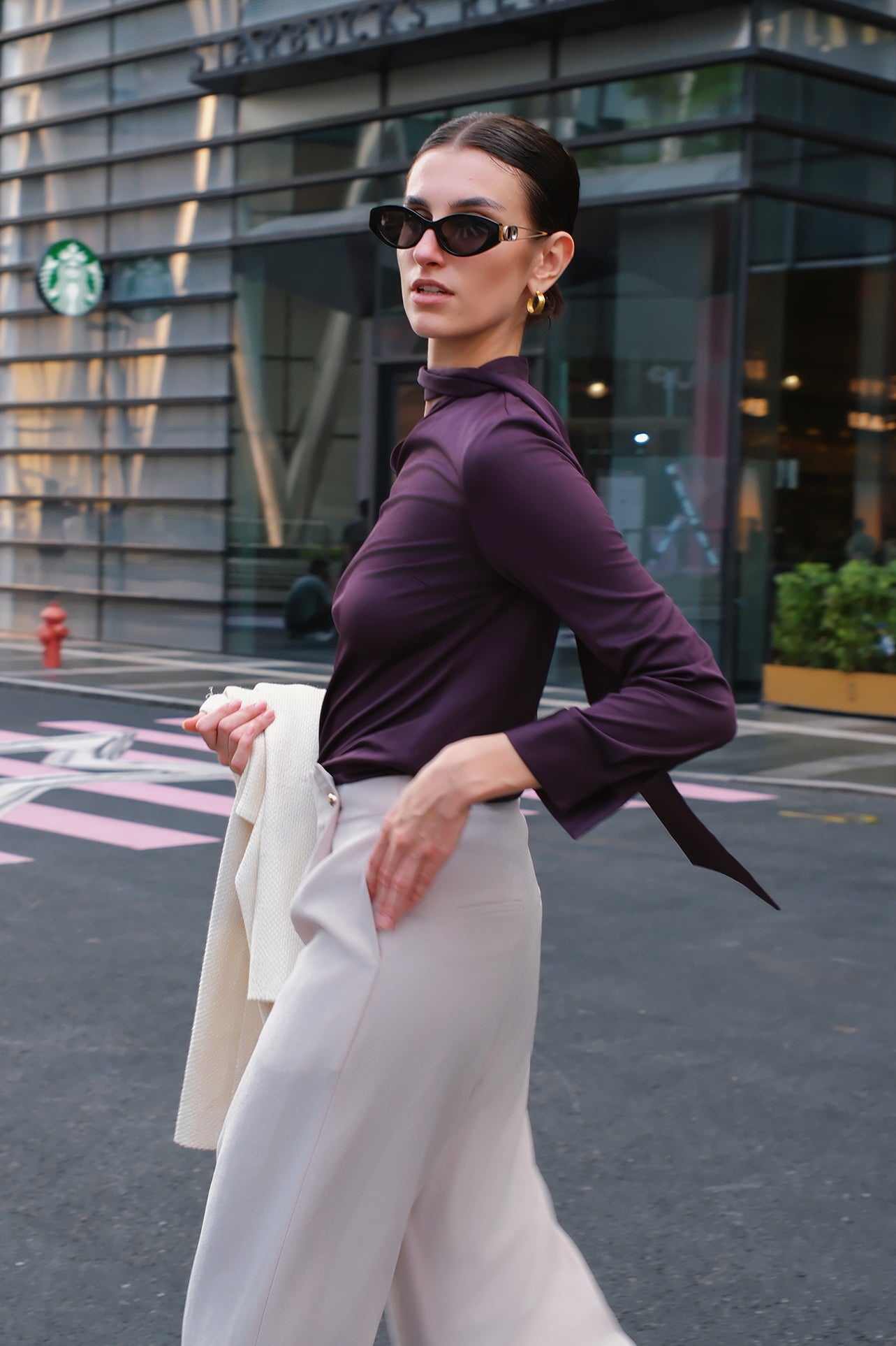 A chic woman wearing an elegant deep plum long-sleeve blouse with an asymmetric high-neck scarf tie, neatly tucked into a high-waisted black tweed skirt embellished with subtle sparkling sequins.