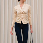 A chic Asian woman modeling an elegant champagne gold long-sleeve top featuring a sophisticated v-neckline and a stylized twist-front knot waist, beautifully paired with high-waisted white trousers.