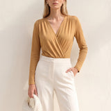 A style comparison of two elegant long-sleeve V-neck wrap tops featuring delicate shoulder pleating and a sleek tucked-in fit; the left in warm camel paired with cream trousers, and the right in deep burgundy paired with black trousers.