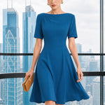 A beautiful model wearing a sophisticated medium blue A-line midi dress featuring an elegant boat neckline with refined asymmetric shoulder pleating, short sleeves, and a flowing flared swing skirt.