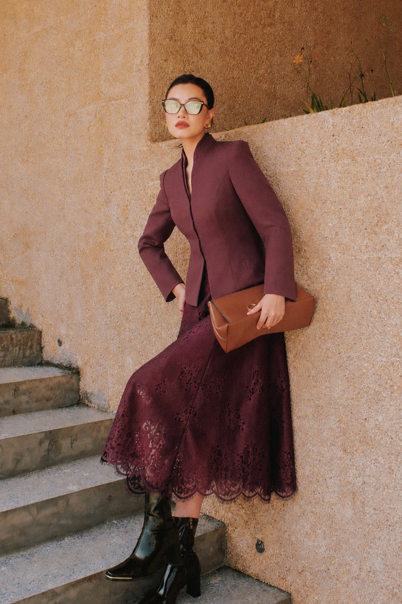 A professional Asian woman wearing glasses and an elegant deep burgundy tailored blazer featuring a sophisticated stand collar with a split V-neckline, structured shoulders, and a clean minimalist front.