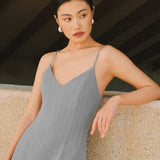 A stylish woman walking on a city street wearing an elegant light grey sheath midi dress with a sophisticated capelet sleeve design, round neckline, and side slit, carrying a black leather handbag.