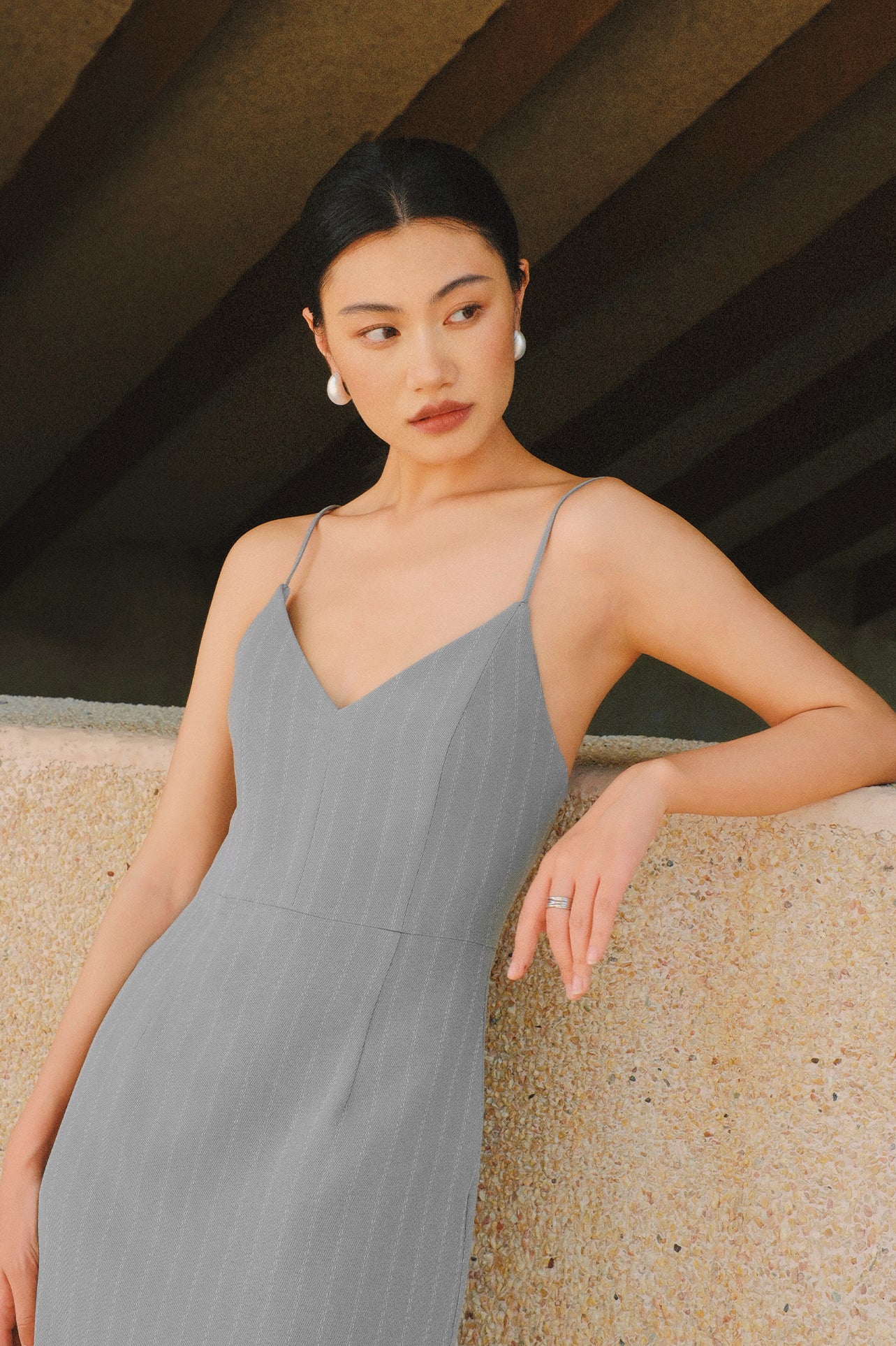 A stylish woman walking on a city street wearing an elegant light grey sheath midi dress with a sophisticated capelet sleeve design, round neckline, and side slit, carrying a black leather handbag.