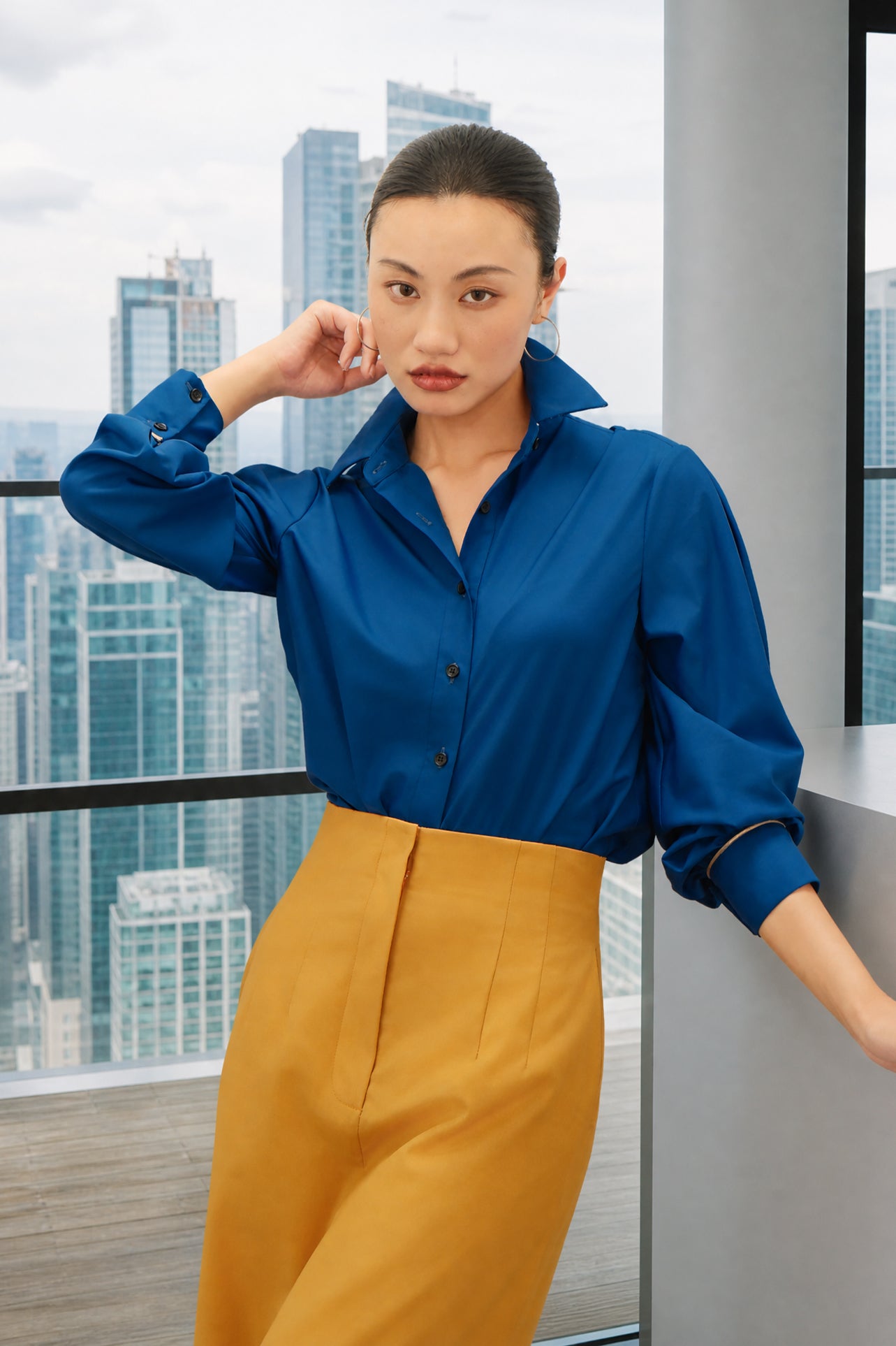 A style comparison of two elegant long-sleeve button-down work shirts with refined cuff stitching; the left in vibrant mustard yellow tucked into a grey pinstripe pencil skirt, and the right in royal blue paired with flowing white wide-leg trousers.