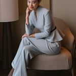 A style comparison of three women wearing tailored two-piece power suits featuring long-sleeve split V-neck jackets with dramatic asymmetrical peplum hems and matching cuffed wide-leg trousers; shown in vibrant crimson red, deep navy blue, and pale ice blue.